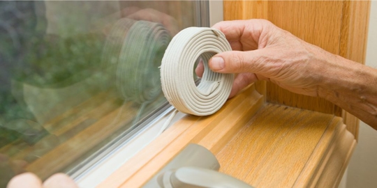 Close up photo of someone's hand weatherstripping a window